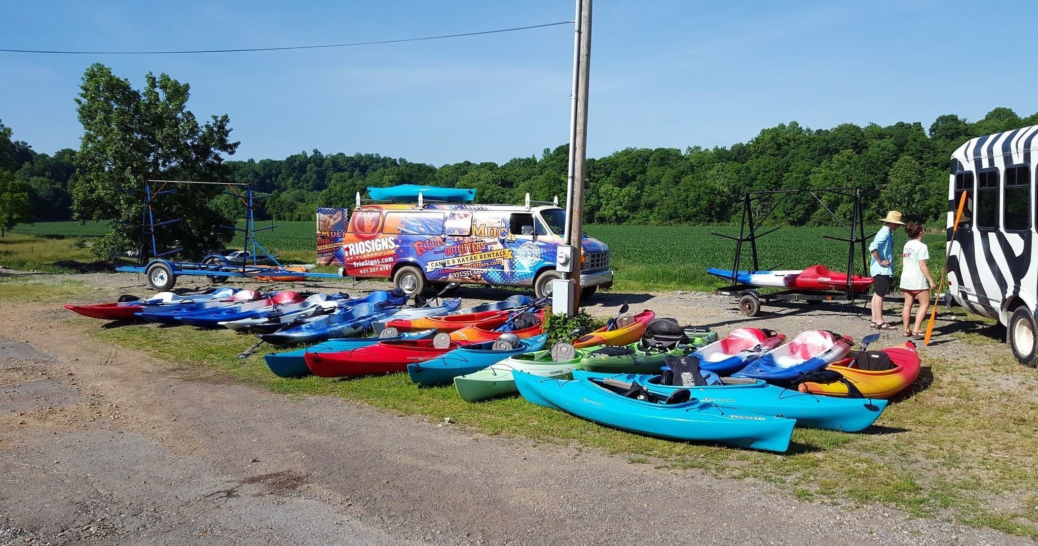 Colorful kayaks lined at riverside rental lot on sunny day
