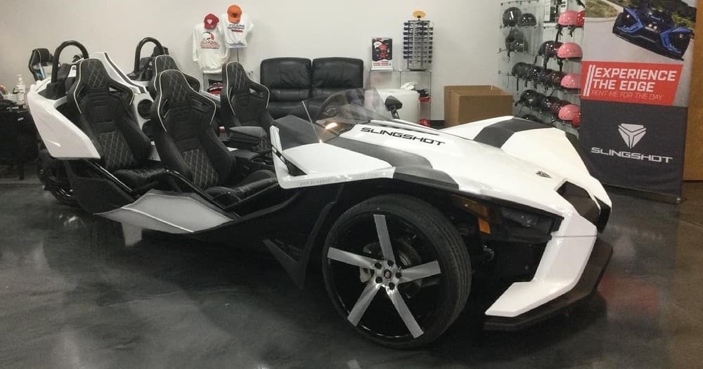 White multi-seat Slingshot parked indoors at rental shop display