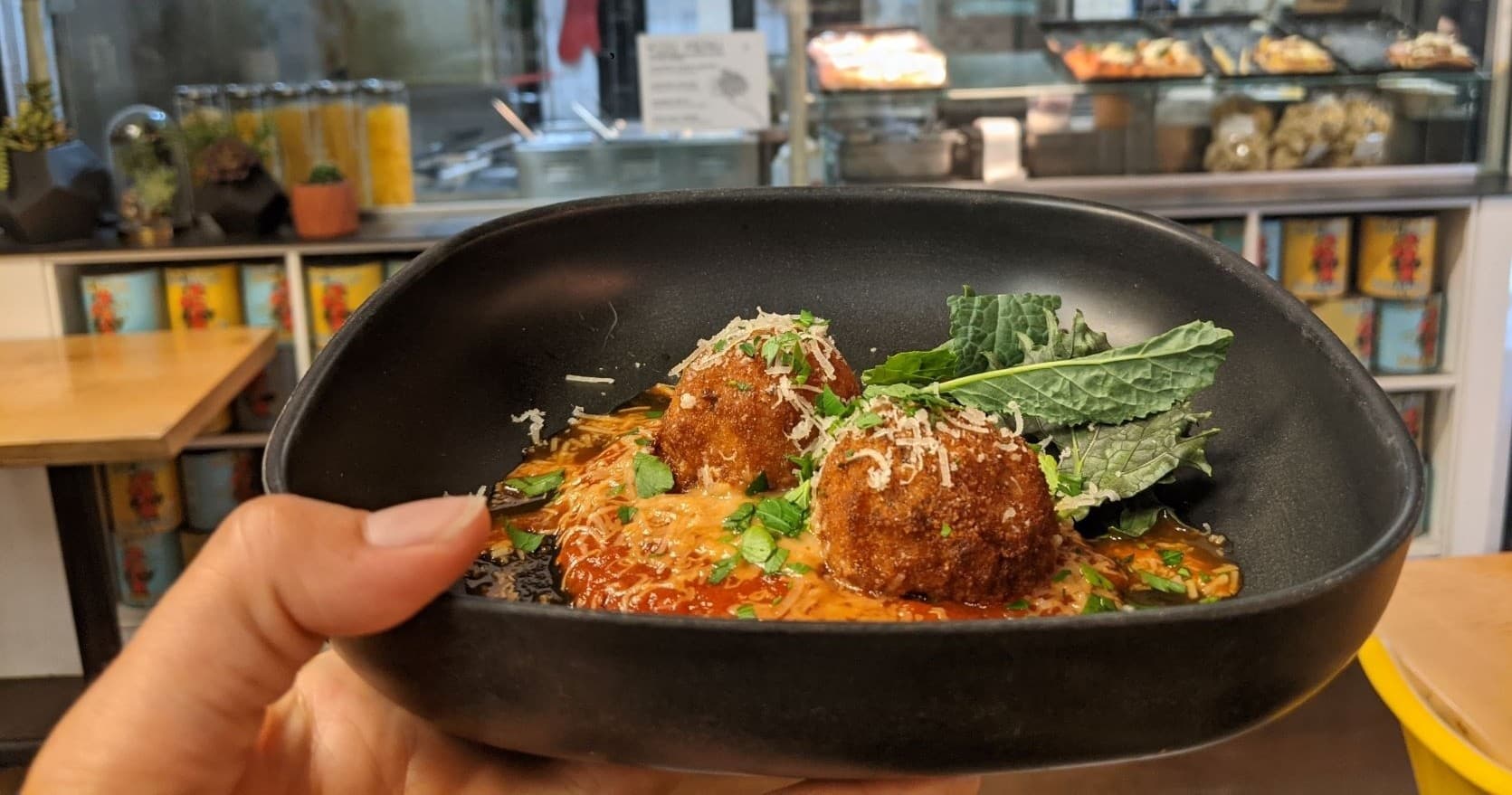 Hand holding gourmet meatballs dish in a casual cafe setting