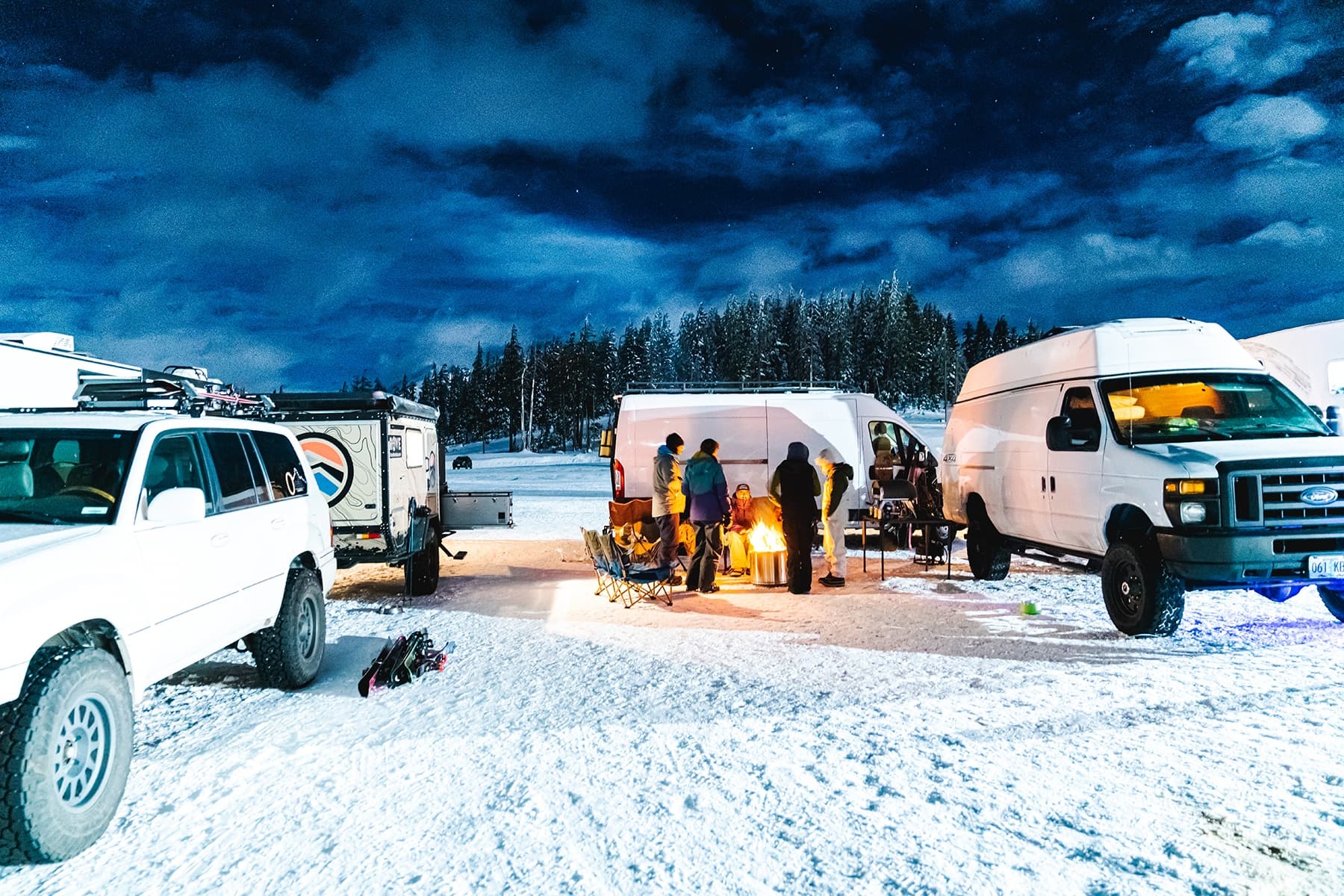 Nighttime winter vanlife gathering at snowy mountain basecamp