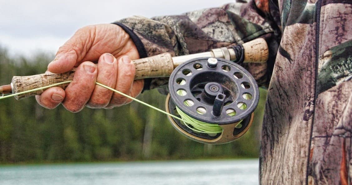 Close-up fly reel and rod held over alpine lake during cast
