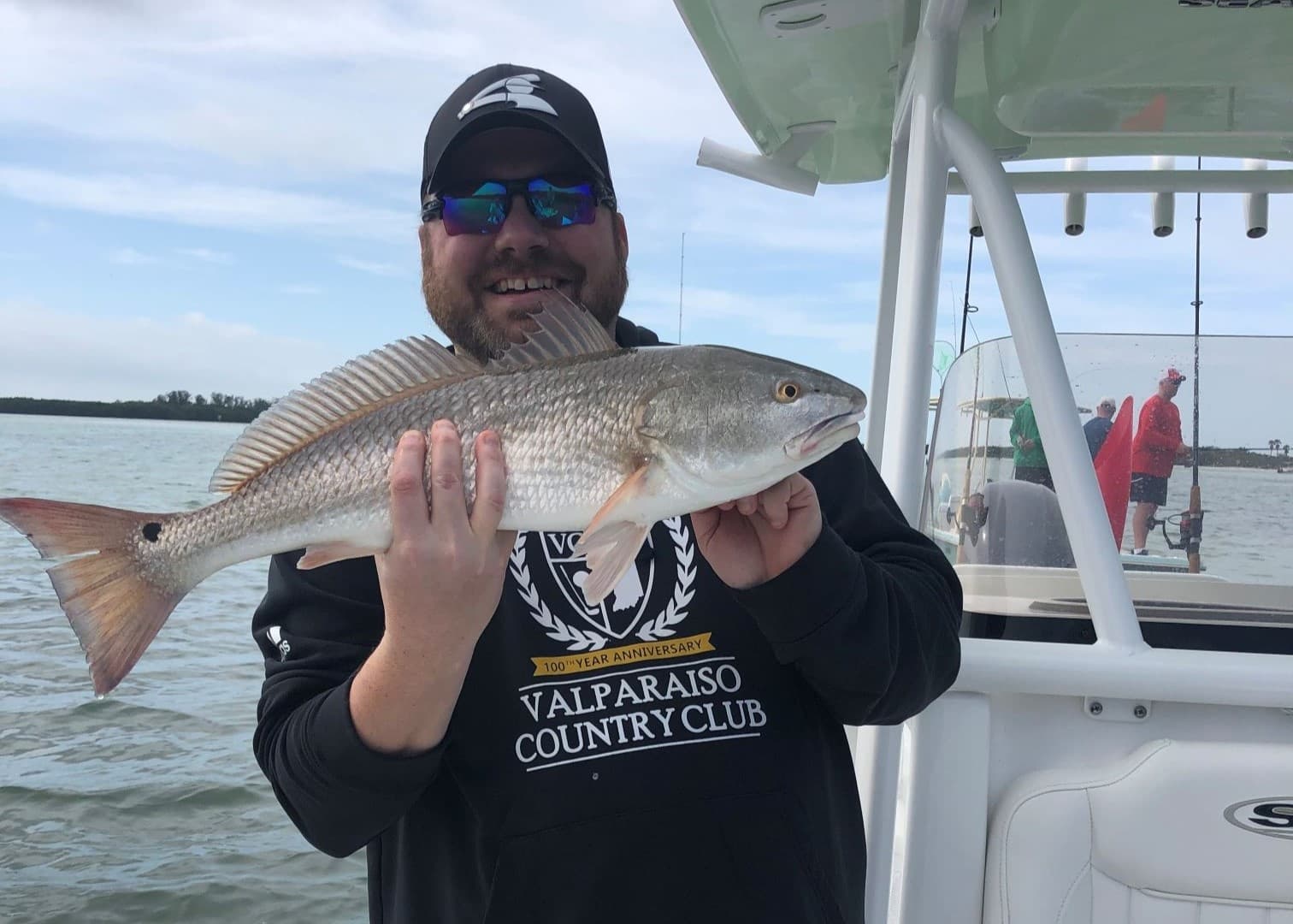 Angler on boat proudly holding large redfish near mangroves