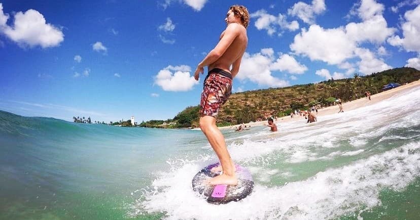Surfer gliding on small wave with tropical Oahu beach backdrop