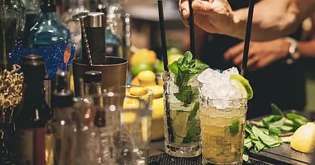 Bartender mixing cocktails at dim indoor bar with fresh garnishes