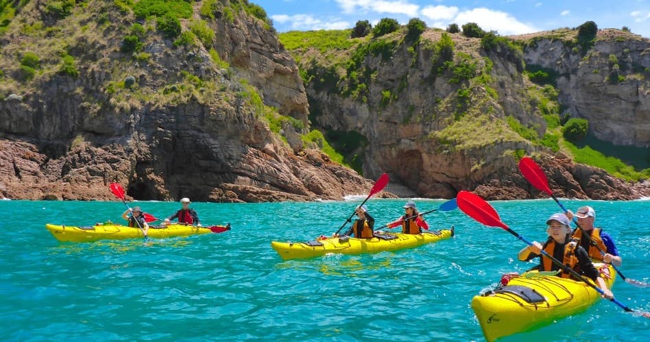 Group kayaking in turquoise waters beside rocky coastal cliffs