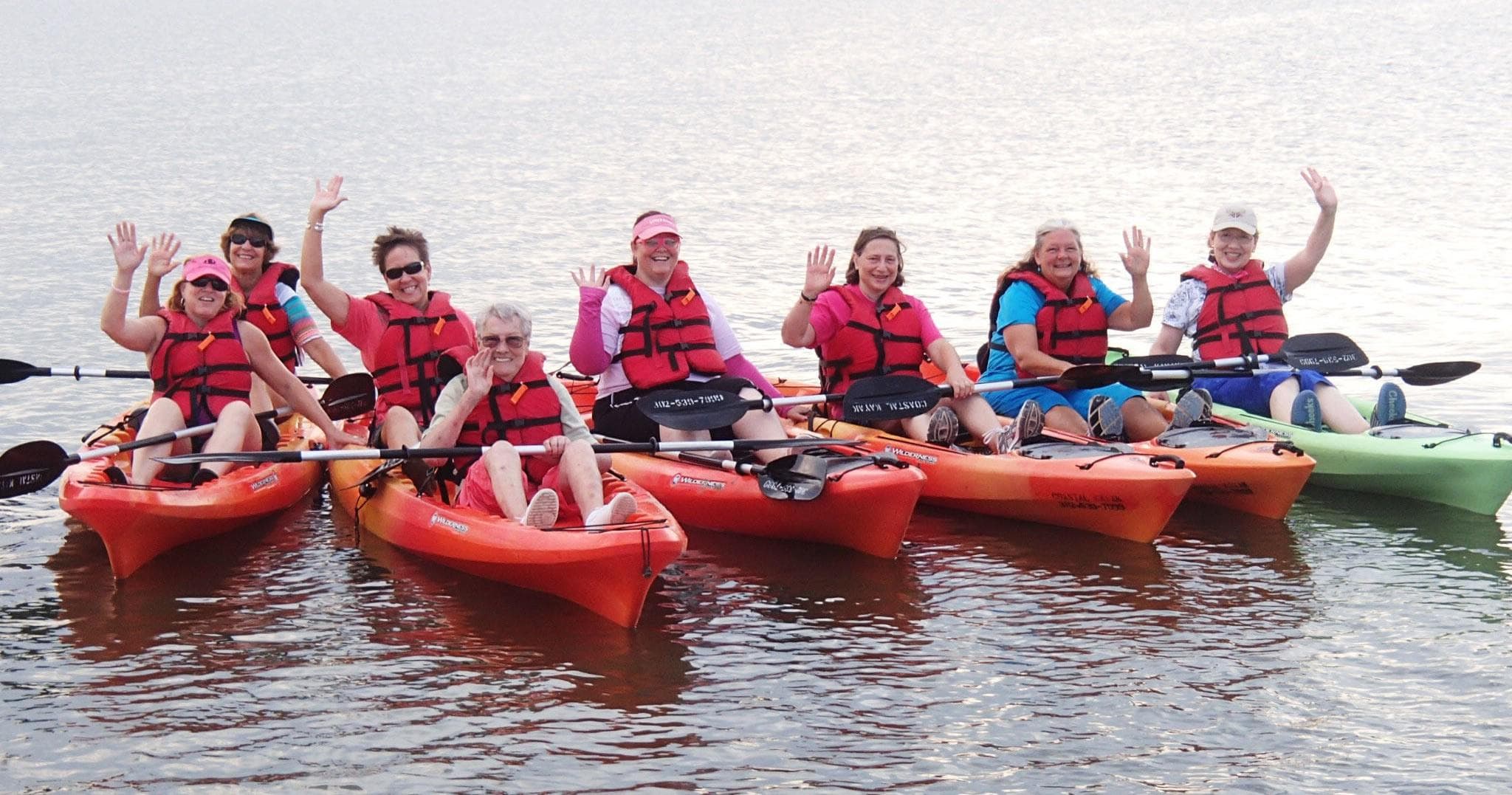 Group sea kayak tour with participants waving in calm coastal waters
