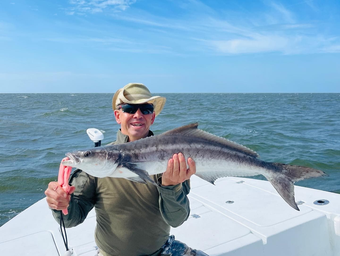 Angler posing with cobia on deck, open ocean backdrop and blue sky