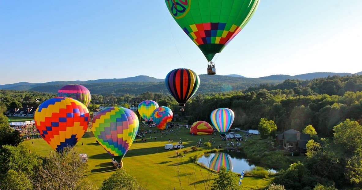 Colorful hot air balloons ascending over green valley festival