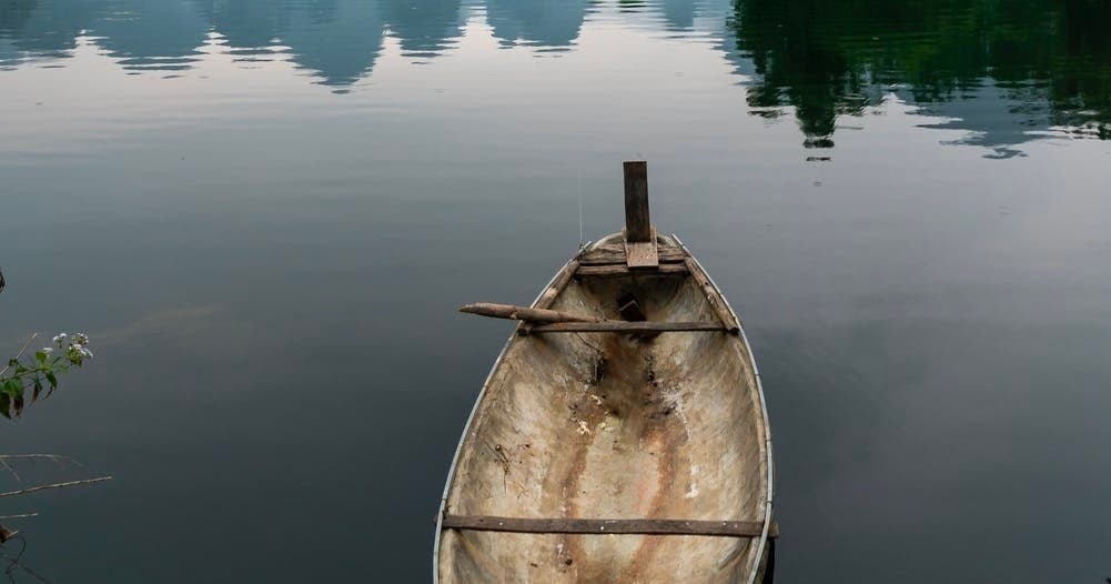 Old wooden rowboat floating on glassy reflective lake water