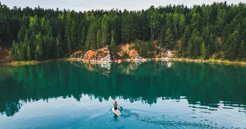 Solo paddler on a turquoise forest lake with mirrored reflections