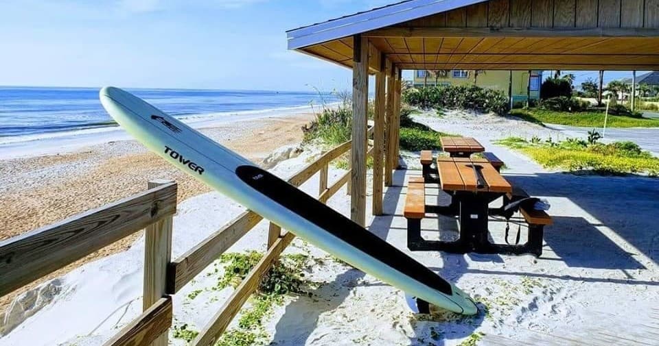 Paddleboard leaned by picnic shelter on sandy beach with ocean view