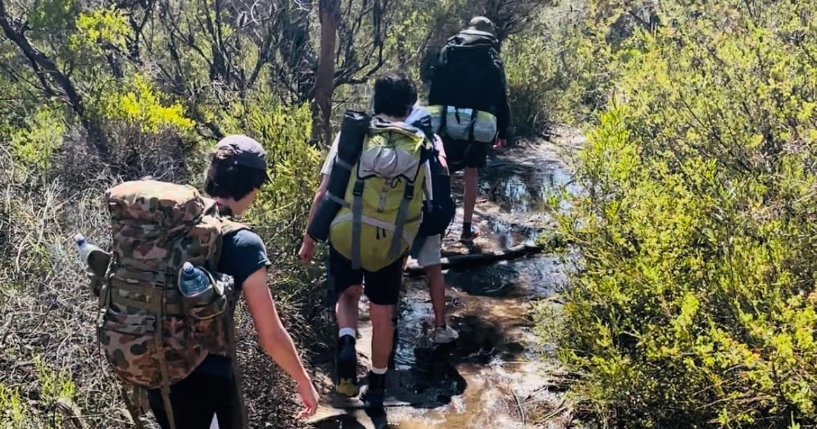Backpackers trekking rocky bush trail through native scrubland outdoors