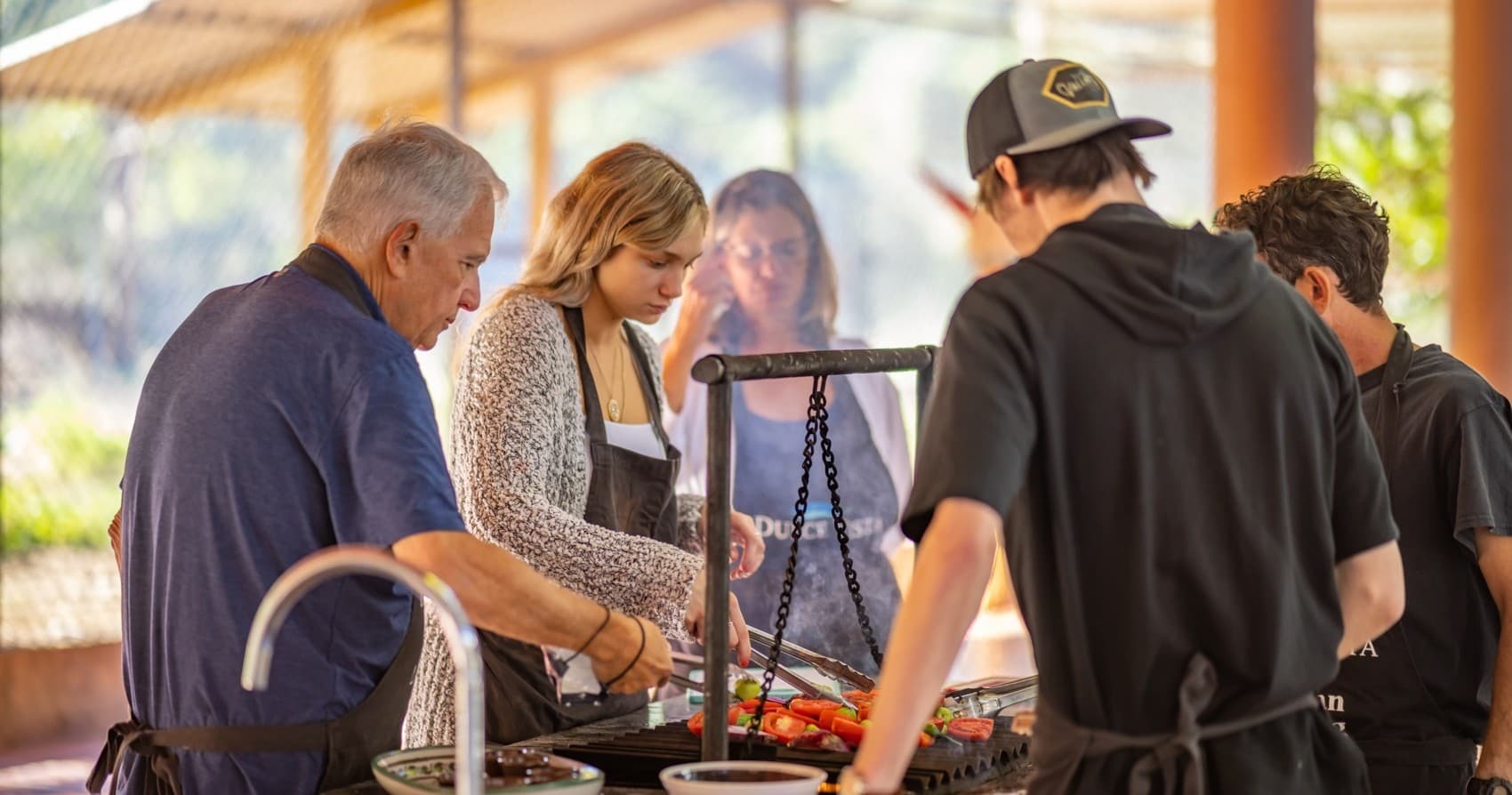 Group grilling cooking class at covered outdoor kitchen with chefs