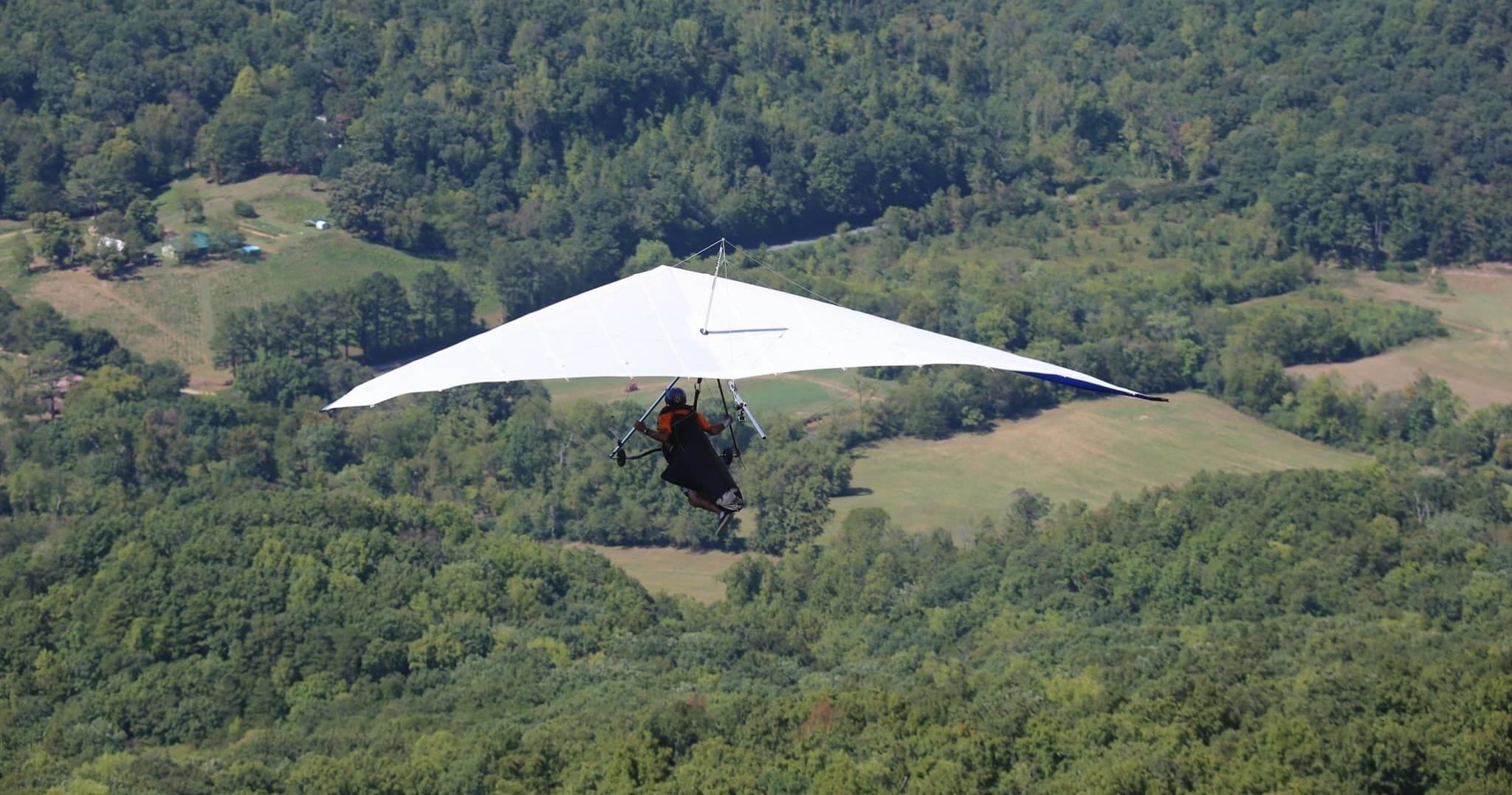 Hang glider soaring over forested valley in scenic aerial flight