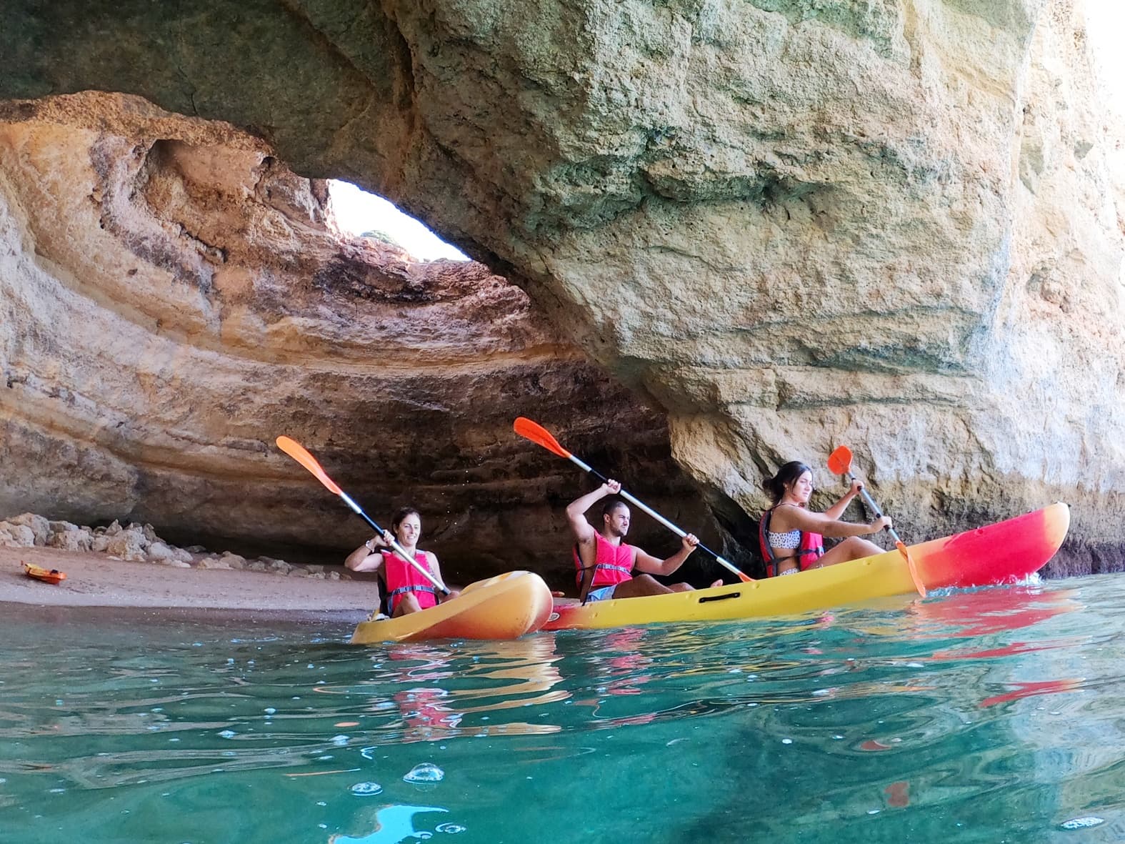 Sea kayakers paddling through coastal cave with turquoise water