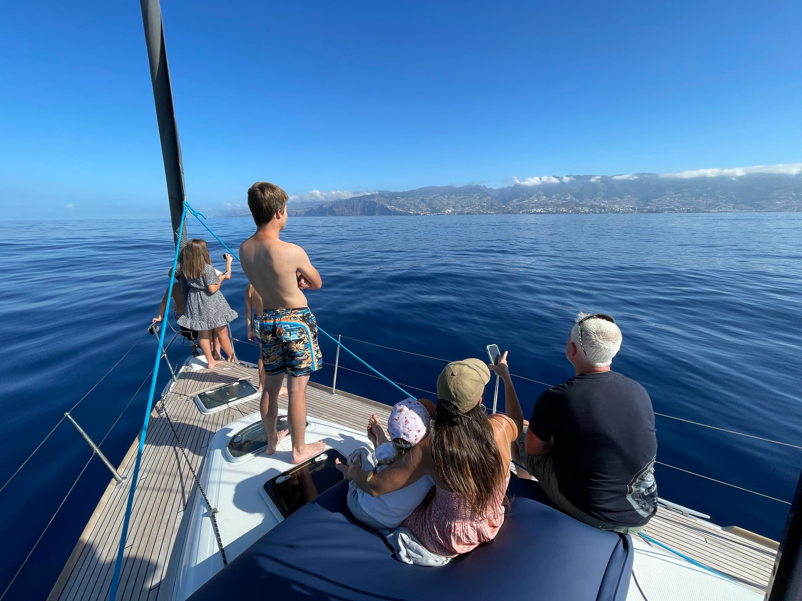 Family on sailboat bow enjoying calm ocean views near coast