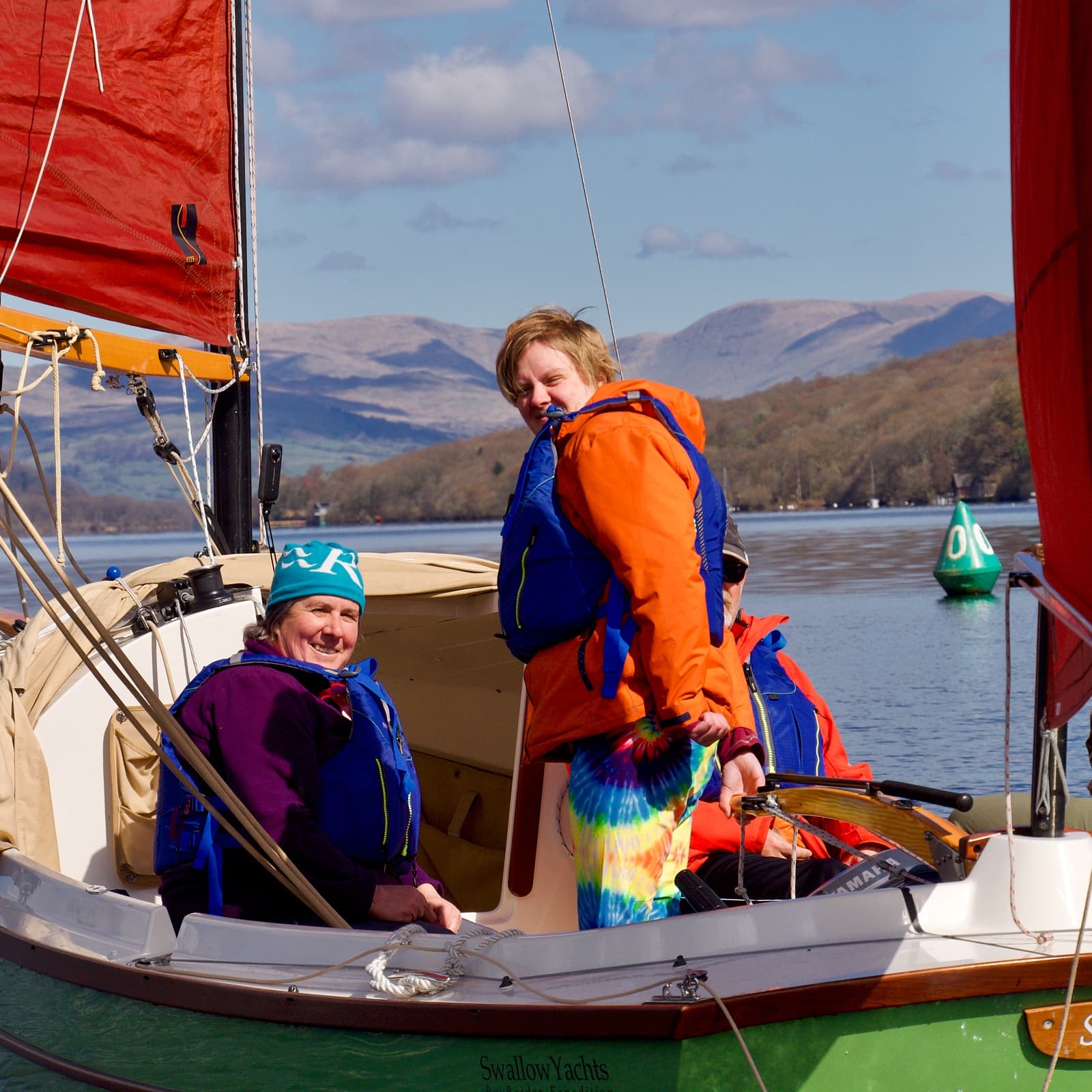 Sailors on a small yacht cruising a scenic lake with hills