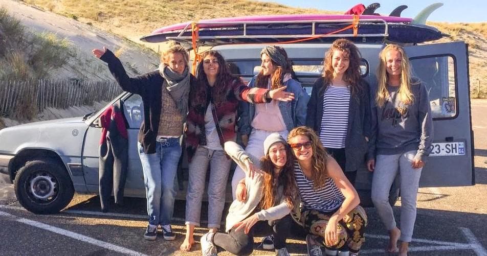 Group of surfers posing by van with roof surfboards at beach parking