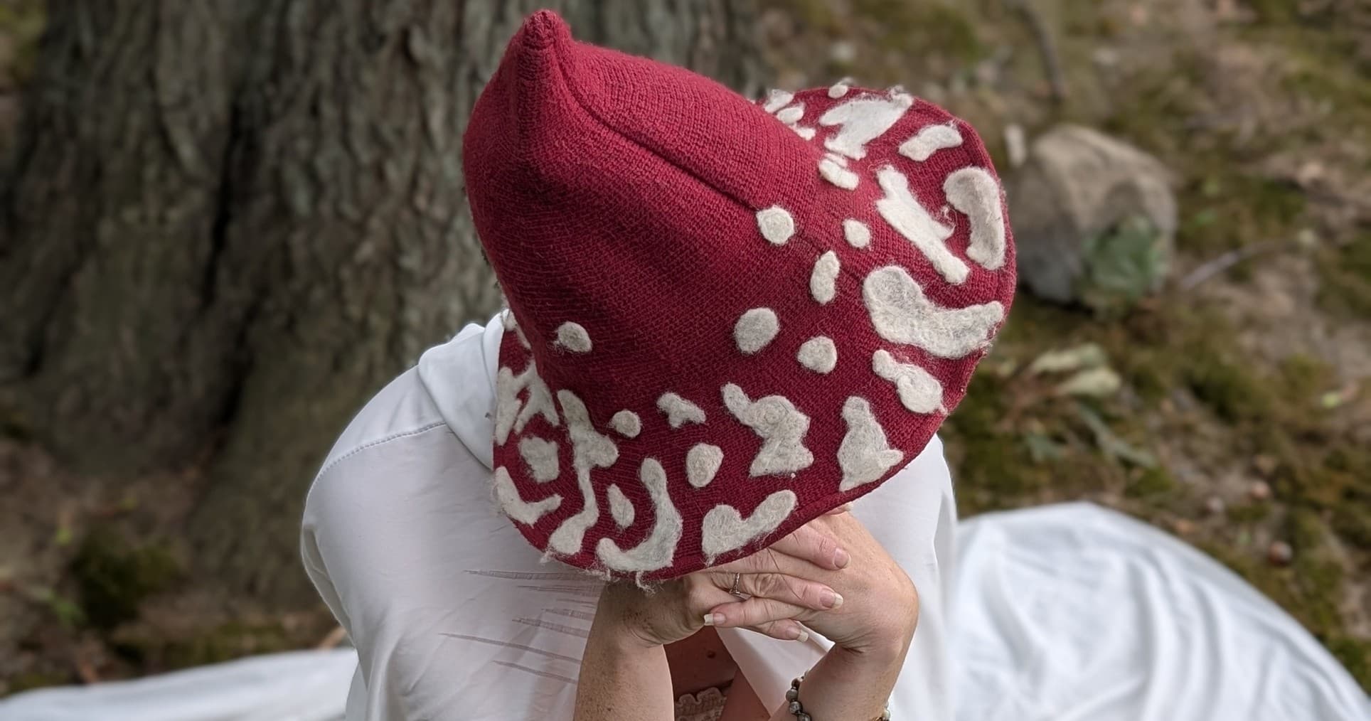 Person in knit hat seated by tree in shaded woodland clearing