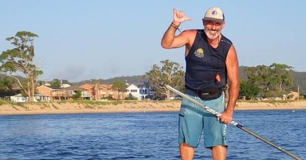 Solo stand-up paddleboarder cruising calm coastal waters, smiling
