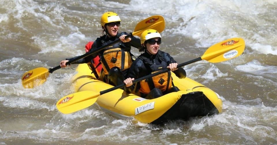 Two paddlers navigating whitewater rapids in tandem inflatable kayak