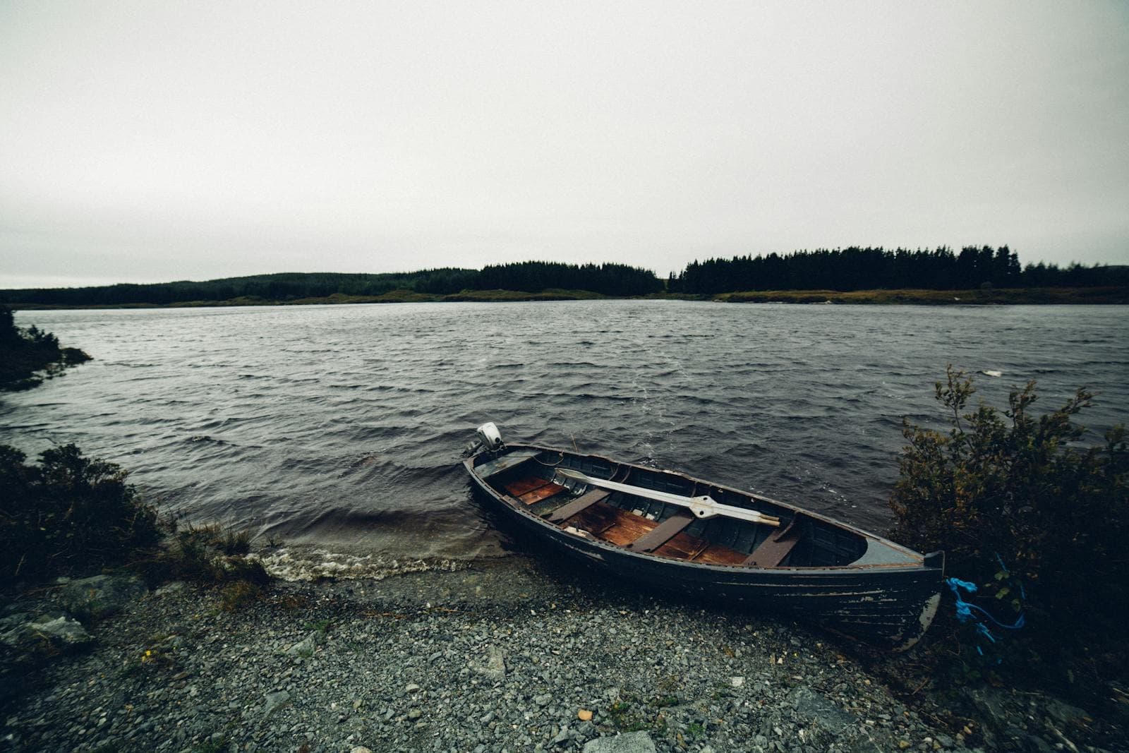 Abandoned rowboat on rocky lakeshore under overcast sky