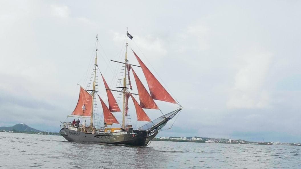 Three-masted schooner under red sails cruising coastal Cartagena waters