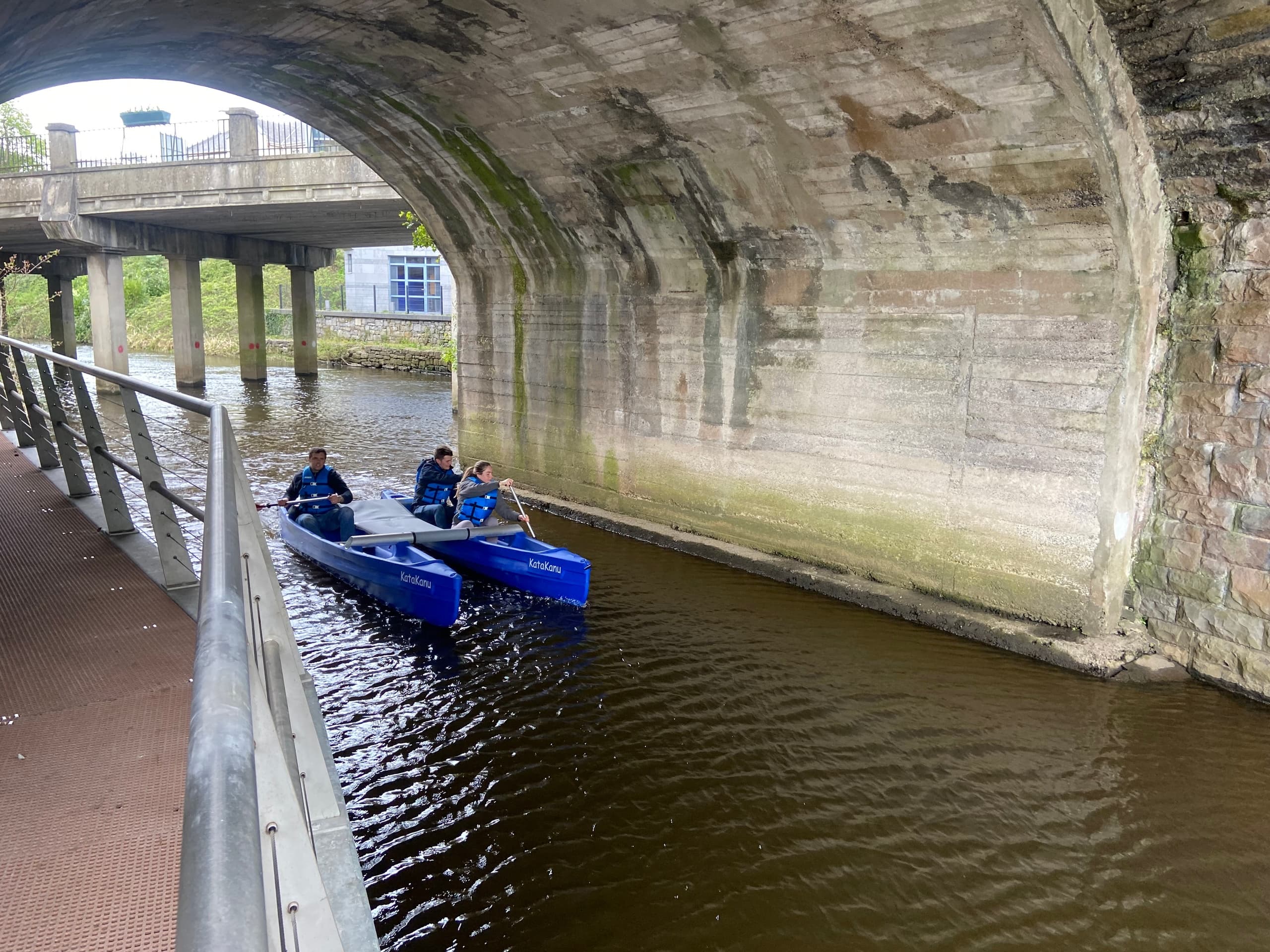 Kayakers navigating under stone bridge along narrow river channel