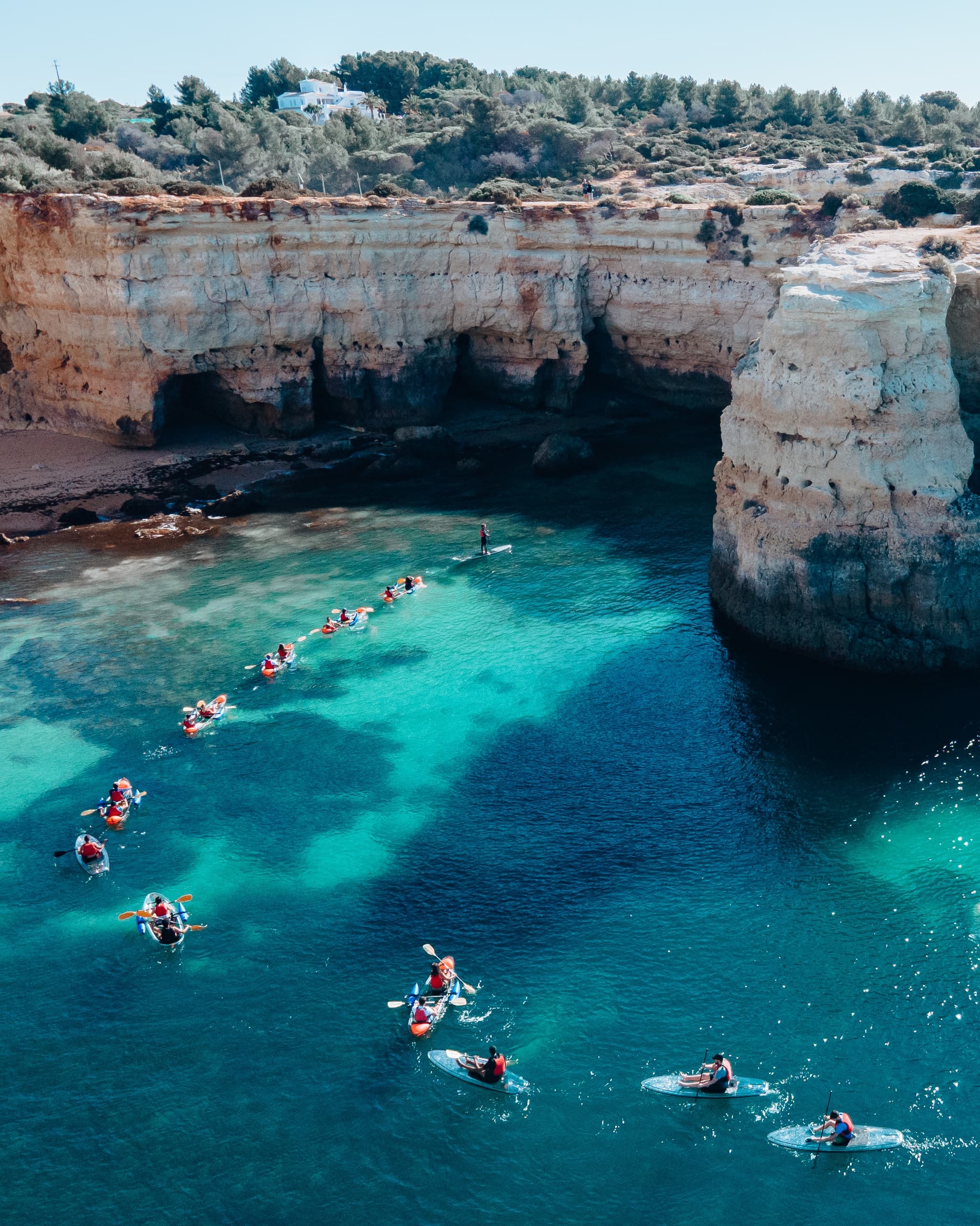 Aerial view of kayakers paddling through turquoise sea near cliffs