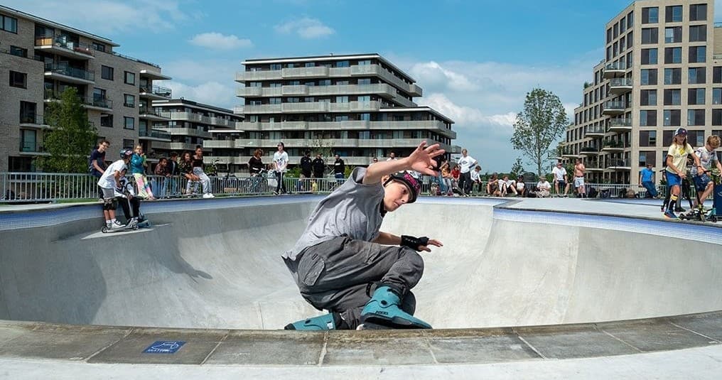 Skateboarder carving in urban concrete bowl with city apartments
