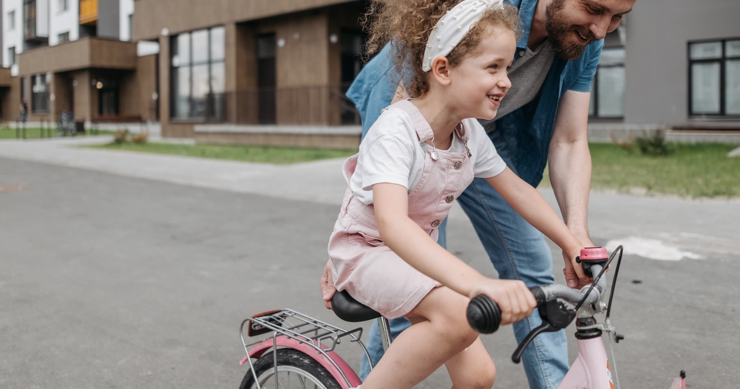 Child learning to ride bicycle with parent on suburban pavement