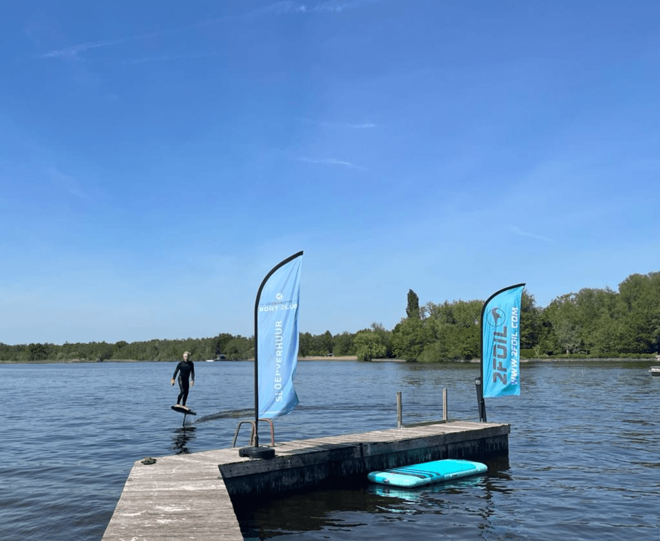 E-foil rider by a dock with brand flags on a sunny lake