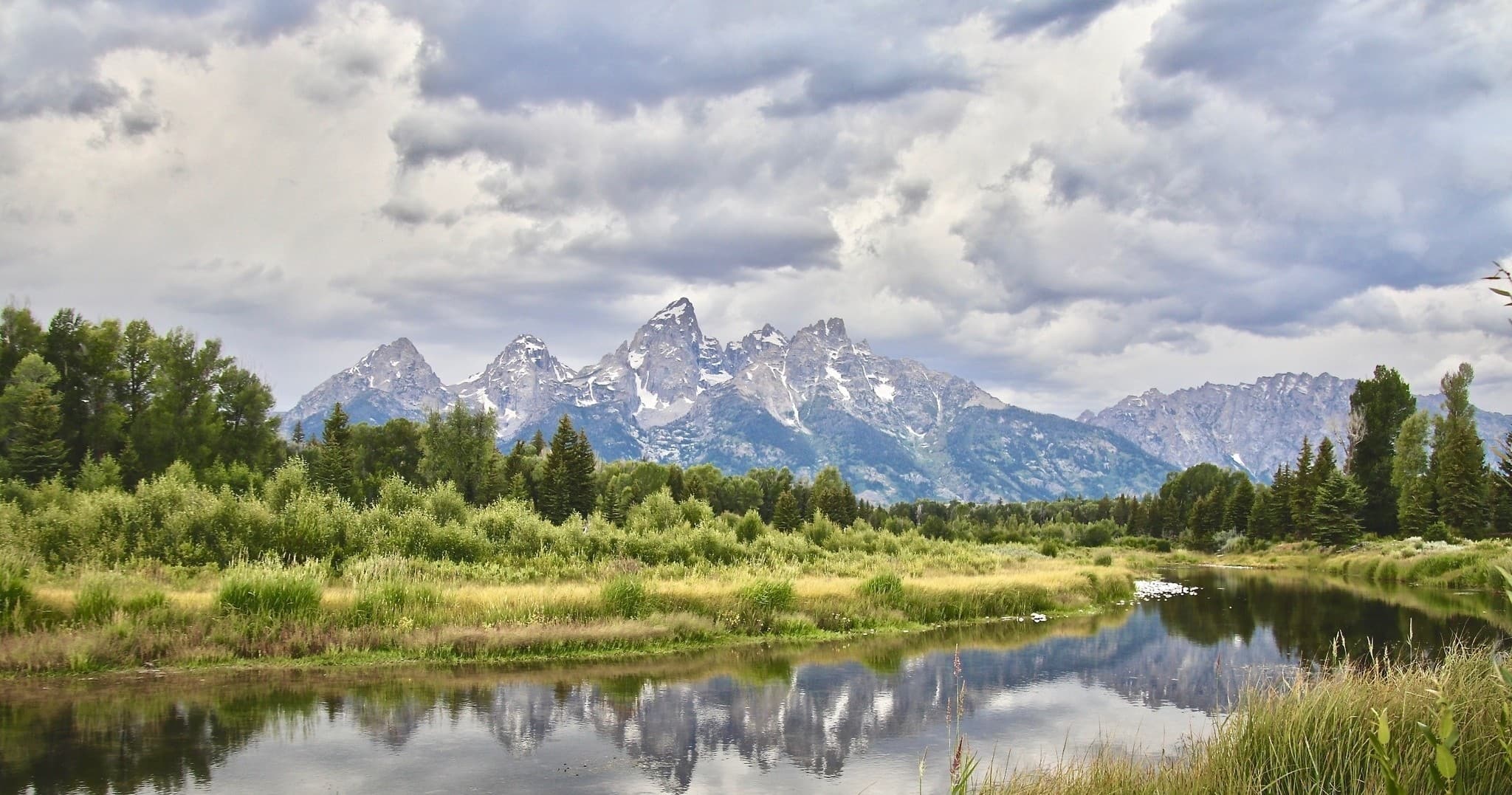 Grand mountain range and meadow reflected in calm river