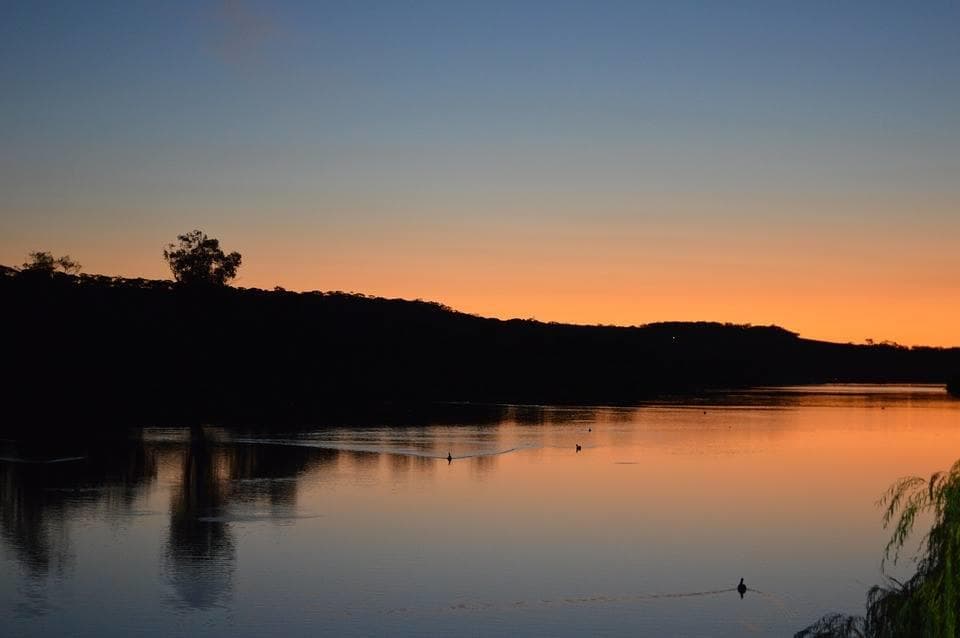 Sunset over Murray River with silhouetted shoreline and calm water