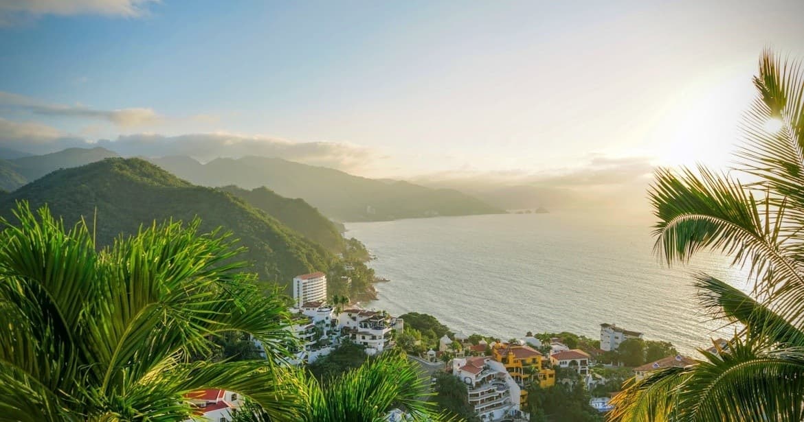 Tropical bay sunrise over coastal town and palm-fringed hills