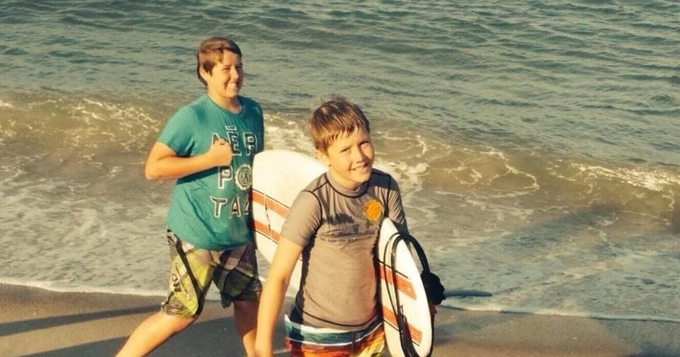 Two boys walking on shoreline holding a surfboard at beach
