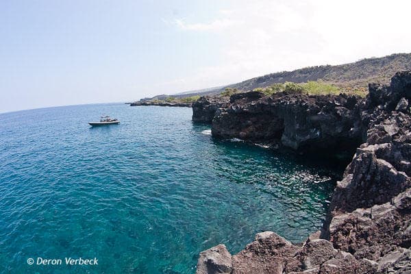 Coastal cliff snorkeling tour boat off rugged Hawaiian shoreline