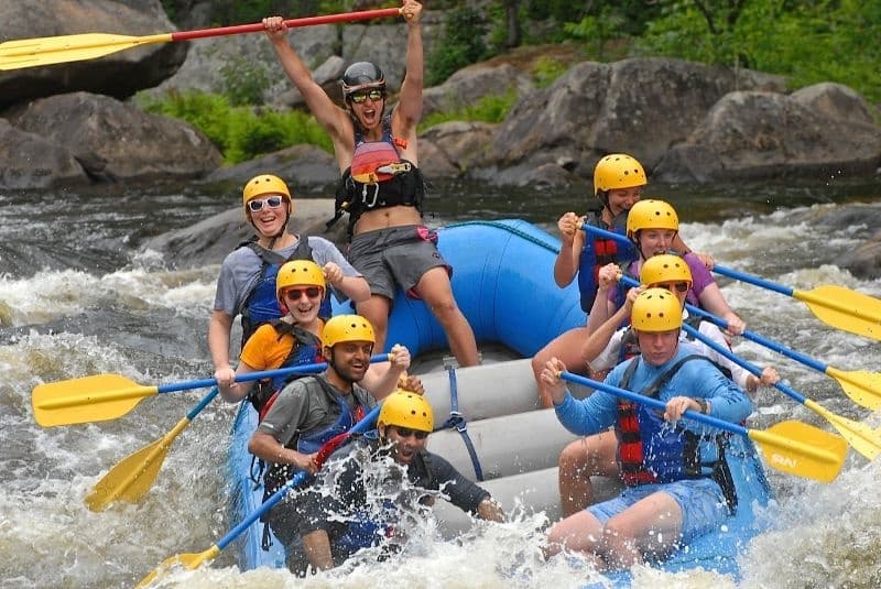 Whitewater rafters paddling through rocky river rapids in summer