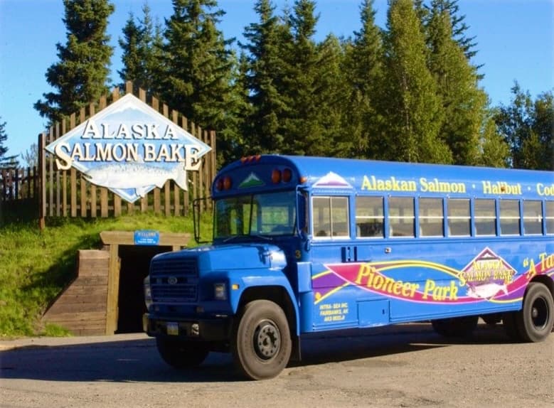 Blue tour bus for Alaska Salmon Bake parked near wooded park