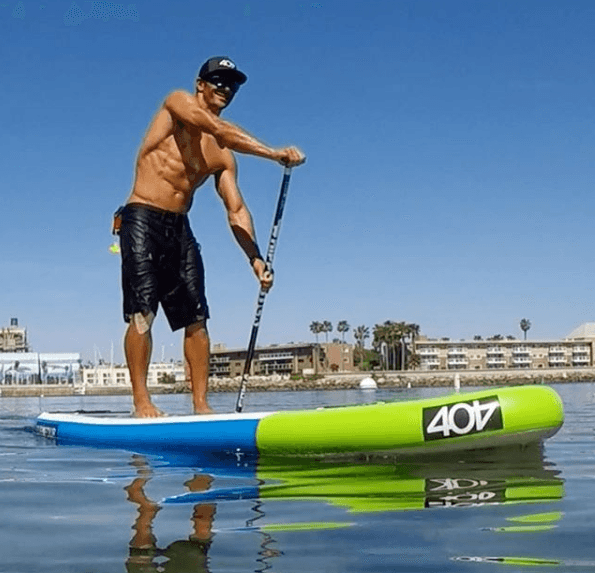 Paddleboarder gliding past sandy shore with clear blue sky