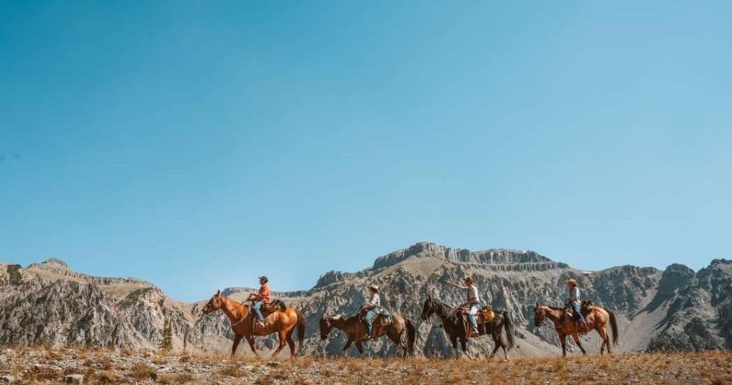Wide horseback pack train crossing open prairie with mountains