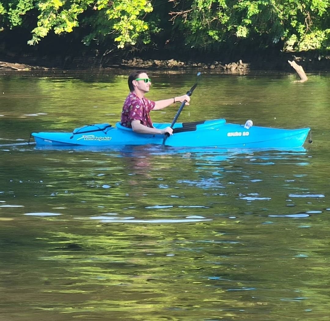 Solo kayaker paddling on calm river surrounded by green trees