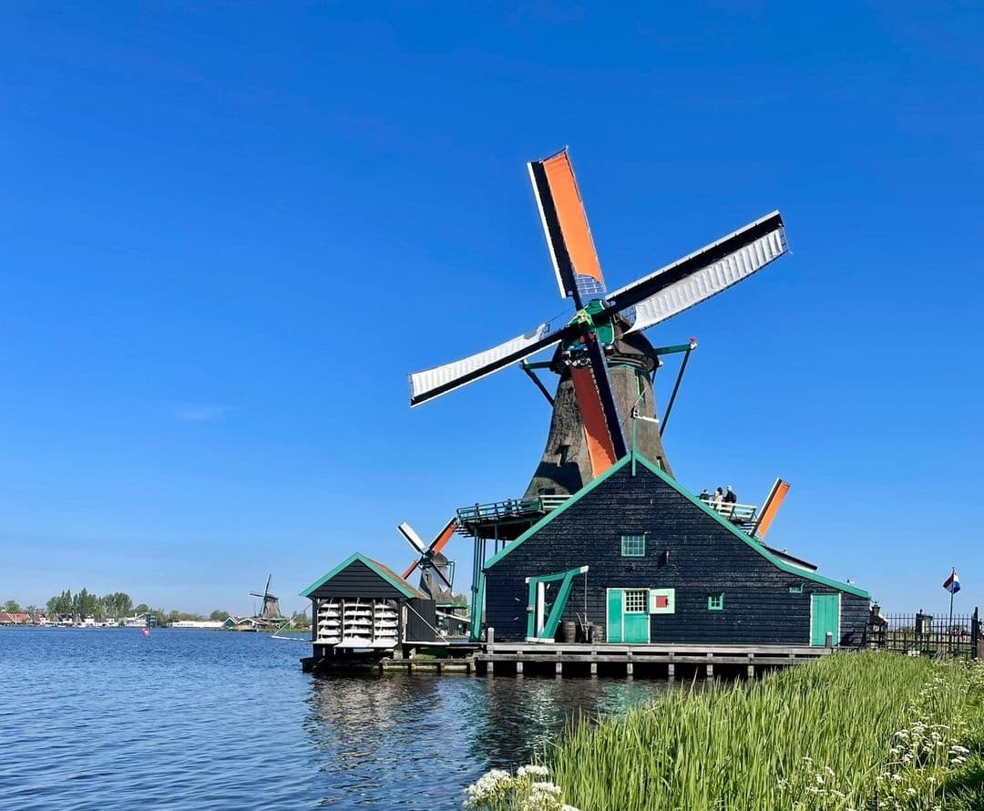 Traditional Dutch windmill by waterfront under blue sky for tours