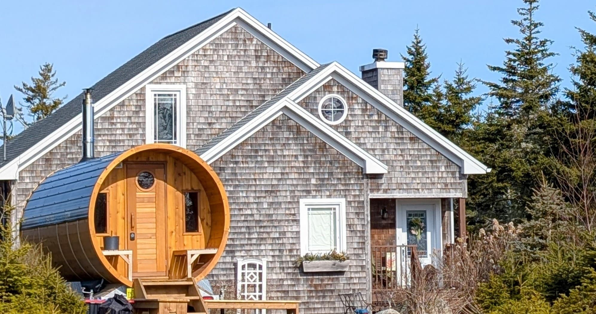 Barrel sauna adjacent to seaside cottage yard for outdoor warmth
