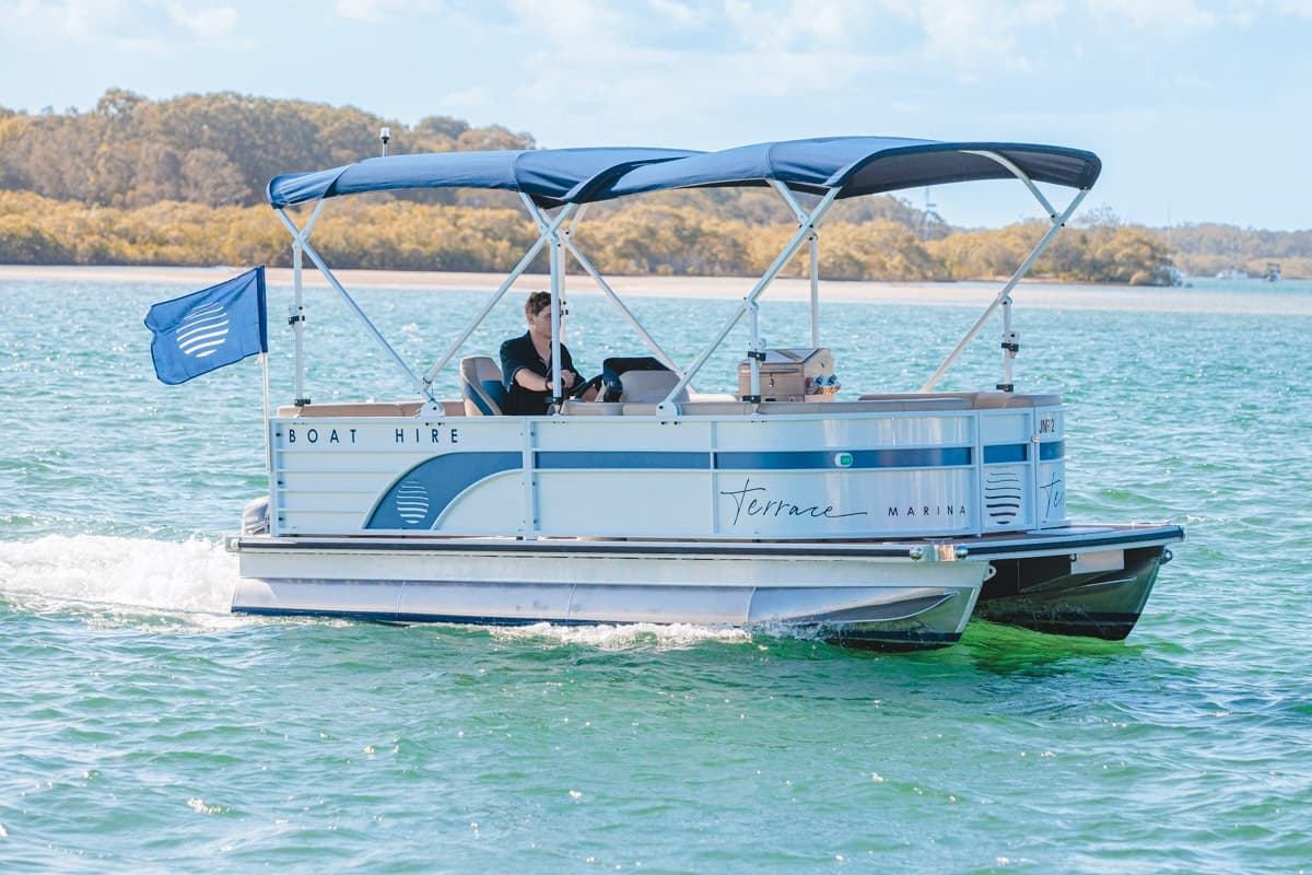 Pontoon boat cruising on blue coastal waters near marina