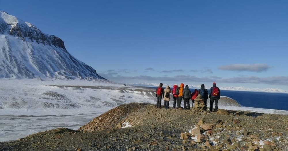 Hikers standing on rocky Arctic coast with glacial mountains