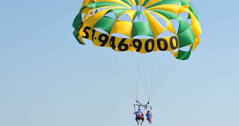 Tandem parasailers under colorful parachute over ocean skyline