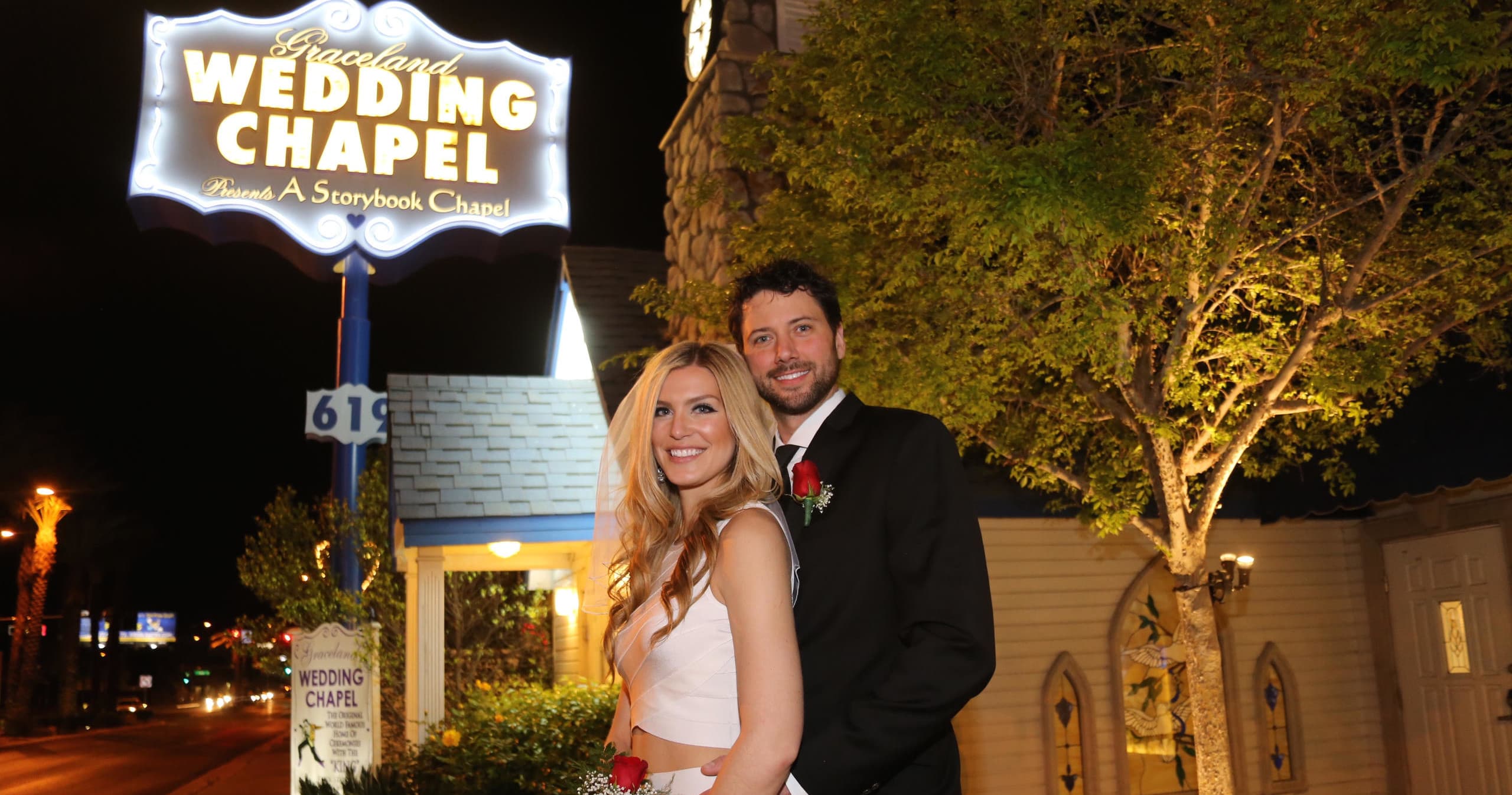 Couple posing by illuminated wedding chapel sign at night