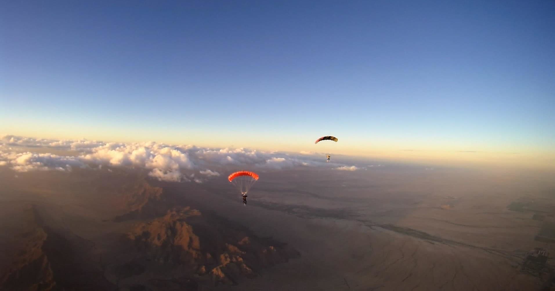Two parachutes soaring above desert mountains and clouds