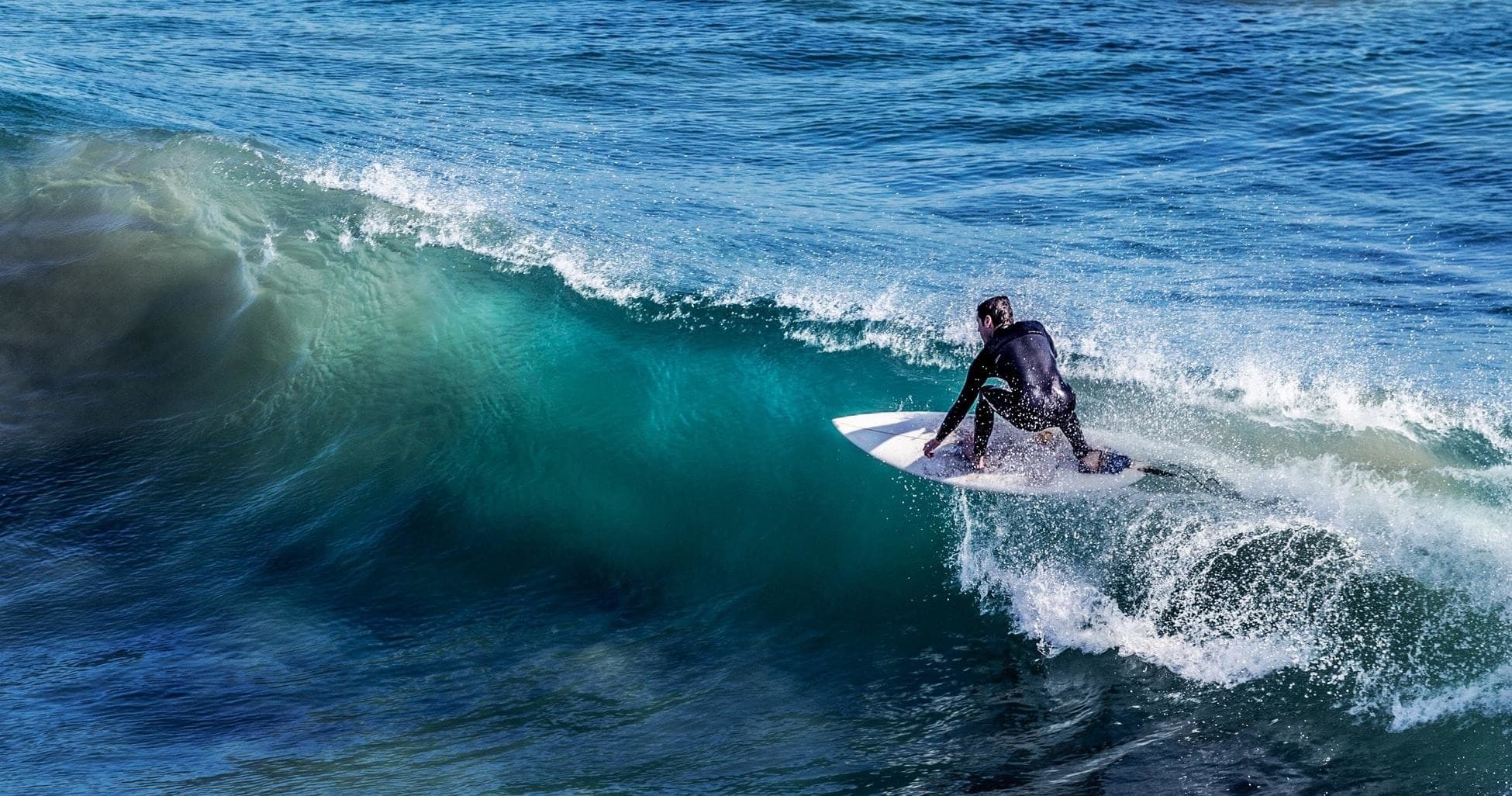 Surfer carving a blue wave off the rugged Scottish coastline